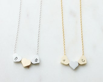 May include: Two silver necklaces with three heart-shaped charms. The charms are engraved with the letters B, W, and a blank heart on one necklace, and A, C, and a blank heart on the other necklace.
