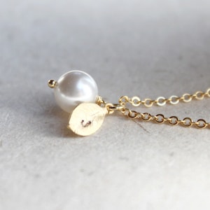 May include: A gold chain necklace with a single white pearl and a gold leaf charm with the letter "C" engraved on it.
