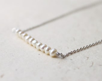 May include: A delicate silver chain necklace with a row of small white pearls.
