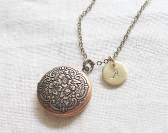 May include: A gold chain necklace with a round locket pendant featuring a floral design and a smaller round charm with the letter 'A' engraved on it.