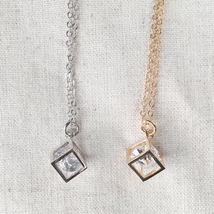 Op de afbeelding: Twee delicate kettingen met een kubische zirkonia-steen in een vierkante zetting. De ene ketting is zilver en de andere is goud.