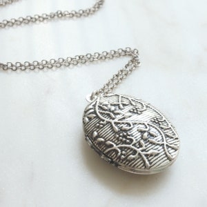 May include: A silver chain necklace with an oval locket pendant. The locket features an intricate floral design.