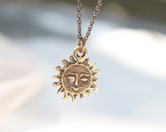 May include: A gold necklace with a sun pendant. The sun has a face with a closed eye and a frown.