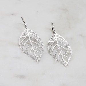 May include: A pair of silver leaf-shaped earrings with a delicate, intricate design. The earrings are dangle style and have a simple hook fastening.