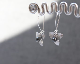May include: A pair of silver dangle earrings with a black bead and a flower design.