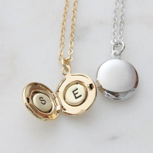 May include: Two gold locket necklaces with initial charms. The locket on the left is open and reveals the letter "S" inside. The locket on the right is closed and has the letter "E" engraved on the front.