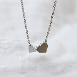 May include: A silver necklace with two heart-shaped pendants. The larger heart is on the right and the smaller heart is on the left.