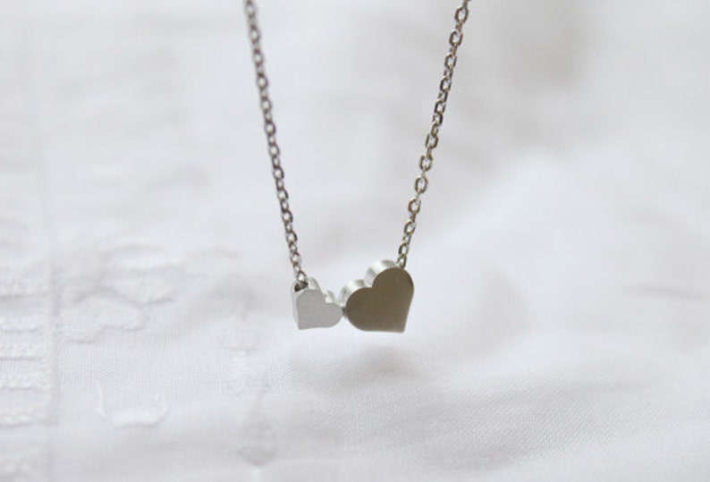 May include: A silver necklace with two heart-shaped pendants. The larger heart is on the right and the smaller heart is on the left.