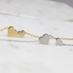 May include: Two delicate necklaces with heart-shaped pendants. One necklace features two gold hearts, while the other has two silver hearts.