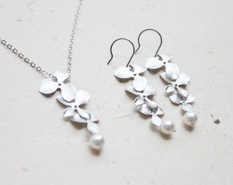 May include: A silver necklace and earrings set featuring a delicate floral design with a single pearl pendant. The necklace and earrings are made of silver and feature a cluster of small, delicate flowers.