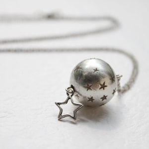 May include: A silver necklace with a round pendant featuring a star pattern. The pendant is attached to a silver chain with a small star charm.