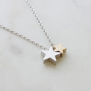 May include: A silver chain necklace with two star-shaped pendants. The larger star is silver and the smaller star is gold.