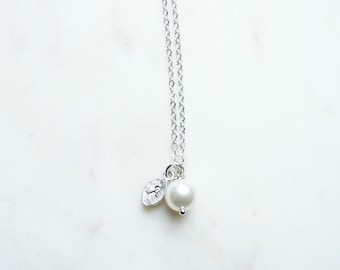 May include: A silver chain necklace with a small silver leaf charm and a white pearl pendant.
