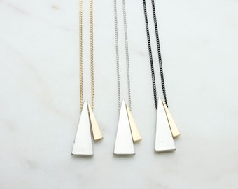May include: Three silver triangle pendant necklaces with a smaller gold triangle accent on each. The necklaces are on a white background.