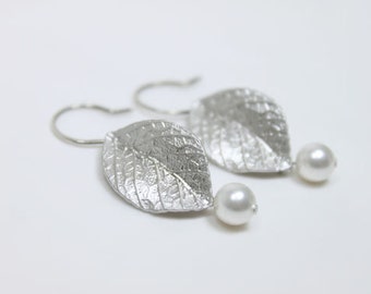 May include: Silver earrings with a leaf design and a pearl dangle. The leaves are textured and have a hammered finish.