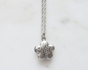 May include: A silver necklace with a flower charm. The charm has a detailed design of flowers and a butterfly.