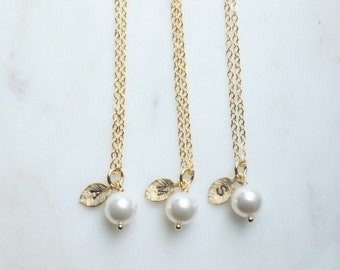 May include: Three gold necklaces with delicate chains and small pearl pendants. Each pendant features a gold leaf charm with a letter engraved on it: A, M, and S.