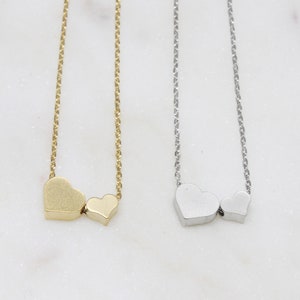 May include: Two delicate necklaces with heart pendants. One necklace is gold with two heart charms, the other is silver with two heart charms.