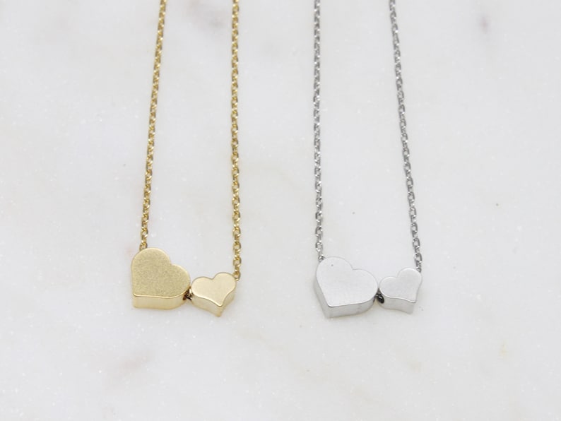 May include: Two delicate necklaces with heart pendants. One necklace is gold with two heart charms, the other is silver with two heart charms.