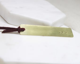 May include: A gold bookmark with a brown leather tassel. The bookmark is engraved with the initials "S.M.O."
