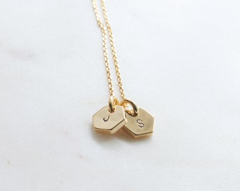 May include: Gold necklace with two hexagonal charms, one with the letter 'J' and the other with the letter 'S'.