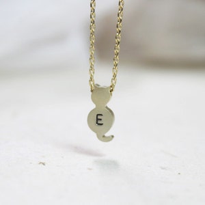 May include: A gold chain necklace with a small, gold, cat-shaped pendant. The pendant has the letter "E" engraved on it.