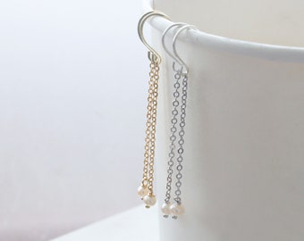 May include: Two pairs of dangle earrings. One pair is gold-toned, the other is silver-toned. Each earring features a delicate chain with small, round, white pearls at the bottom. The earrings are hanging against a white background.