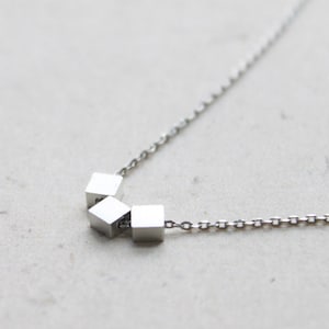Könnte beinhalten: Eine silberne Halskette mit einer Kette und einem Anhänger aus vier kleinen silbernen Würfeln.