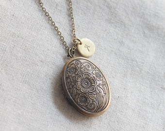 May include: A gold-toned oval locket necklace with a floral design. The locket has a hinged opening and is attached to a delicate chain. A small gold-toned charm with the letter "A" is attached to the chain above the locket.