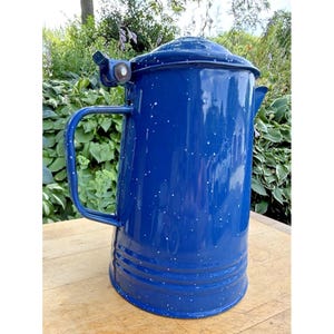 May include: A vintage blue enamelware coffee pot with a lid, handle, and spout. The cobalt blue pot has white speckles and is set against a natural background. This classic camping or kitchenware item is ideal for brewing coffee or tea.