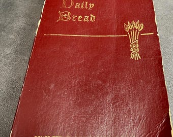 May include: A dark red book titled My Daily Bread with gold lettering and a gold wheat stalk illustration on the front cover. The bottom of the cover features the text CONFRATERNITY OF THE PRECIOUS BLOOD in gold, with visible wear along the edges.