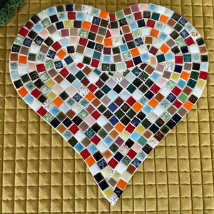 May include: A heart-shaped mosaic piece constructed from numerous small, square tiles in a diverse array of colors including orange, blue, red, green, white, and brown. The tiles are arranged in a grid pattern, forming a solid heart shape.