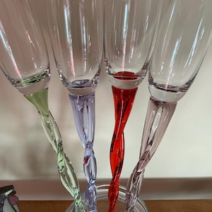 Peut inclure: Quatre flûtes à champagne en verre transparent avec des pieds hauts, fins et torsadés de couleurs distinctes. Les pieds sont vert clair, violet clair, rouge vif et rose pâle. Chaque flûte présente un bol lisse et un pied en spirale.