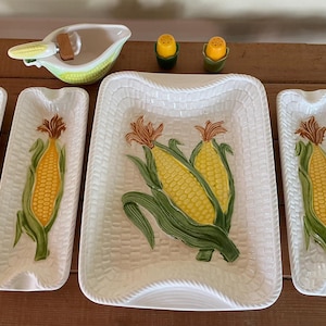 Peut inclure: Un ensemble de vaisselle en céramique sur le thème du maïs comprenant un grand plat de service rectangulaire, quatre plats rectangulaires longs et étroits, une saucière avec une louche en forme de maïs et deux petites salières et poivrières jaune et vert.