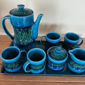 Peut inclure: Service à thé vintage en céramique dans les tons de bleu sarcelle et de vert. L'ensemble comprend une théière, des tasses, un sucrier et une crémière, le tout disposé sur un plateau rectangulaire. Les pièces ont un motif texturé.