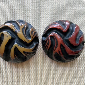 Peut inclure: Deux boutons ronds vintage avec un motif tourbillonnant sculpté. L'un est noir et ambré, l'autre noir et rouge. Ces boutons sont probablement faits d'un matériau dur et conviennent aux projets de couture et d'artisanat.