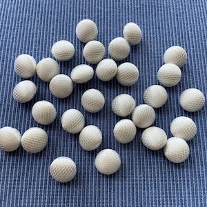 Peut inclure: Plusieurs objets sphériques blancs à texture maillée sont dispersés sur un tissu bleu texturé. Les sphères sont petites, potentiellement décoratives ou fonctionnelles.