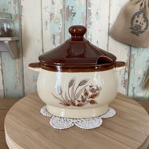以下が含まれることがあります： 茶色の蓋と取っ手が付いた、ヴィンテージのセラミック製スープチューリン。 オフホワイトのボディには、茶色の小麦と花の模様があります。 白いレースのドイリーの上にあり、木製の背景があります。