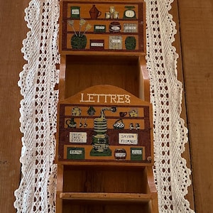 May include: A vertical wooden wall organiser featuring two storage compartments and three bottom hooks. The upper section is labelled FACTURES and the lower section is labelled LETTRES, both decorated with colourful illustrations of kitchen items.