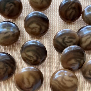 May include: A selection of brown, marble-effect spheres with swirling patterns. The spheres display varying shades of brown and tan, giving a natural, organic look. The spheres are arranged on a light brown surface.