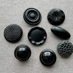 Peut inclure: Divers boutons noirs aux formes et textures variées. Les boutons présentent des motifs tels que des spirales, des motifs floraux et un effet de treillis. Les boutons sont présentés sur un fond en tissu gris. Les boutons sont de tailles et de formes différentes.