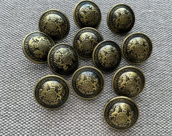 May include: A collection of antique brass-colored buttons. Each button features a detailed embossed design with a central emblem and surrounding decorative elements. The buttons are round and have a slightly aged appearance.