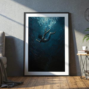 Puede incluir: Impresión artística enmarcada que representa a una persona sumergida en agua azul oscura, con los brazos extendidos. La obra de arte tiene un estilo texturizado y pictórico. La impresión se exhibe en una habitación con una pared gris, suelo de madera y una mesa auxiliar.