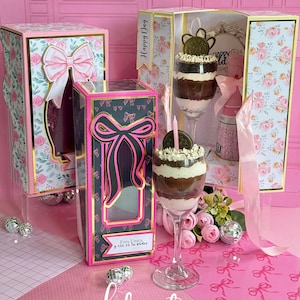 Puede incluir: Cajas de regalo rosas y florales con lazos y un postre en una copa de vino. Las cajas tienen adornos dorados y el texto "Happy Day" y "Eres Unica y ese es tu poder". Elementos decorativos: bolas de discoteca y cintas rosas.