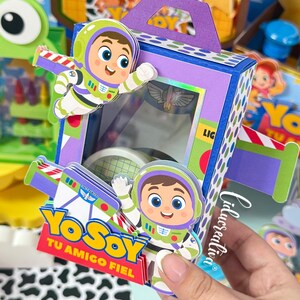 May include: A purple and blue rectangular paper box with a handle, featuring cartoon space ranger characters, green and white accents, and a clear window. The box displays the text "YO SOY TU AMIGO FIEL" in yellow and red lettering on the front.