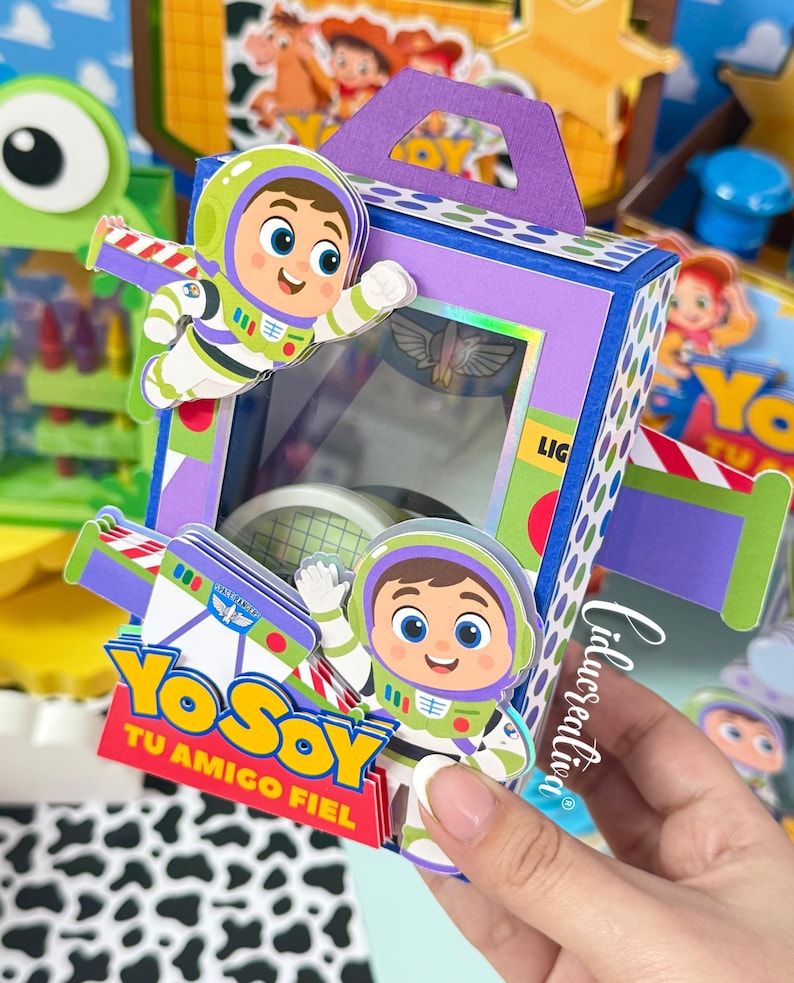 May include: A purple and blue rectangular paper box with a handle, featuring cartoon space ranger characters, green and white accents, and a clear window. The box displays the text "YO SOY TU AMIGO FIEL" in yellow and red lettering on the front.