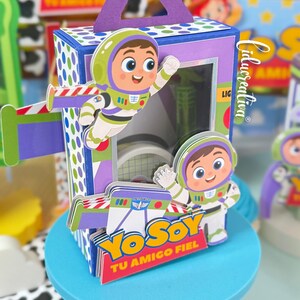 May include: A rectangular purple and blue cardboard favour box featuring a cutout handle and a clear window. The box is decorated with layered paper cutouts of a cartoon space ranger character and the text Yo Soy Tu Amigo Fiel in yellow and red.
