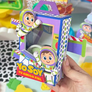 May include: A rectangular purple and blue cardboard box with a handle, featuring cartoon space ranger characters in white, green, and purple suits. The box has a clear window and displays the text Yo Soy Tu Amigo Fiel in yellow and blue letters.
