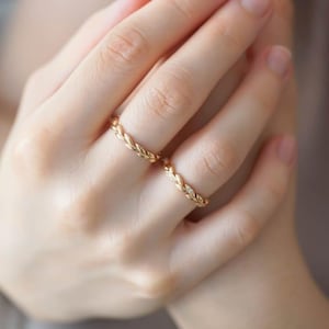 Könnte beinhalten: Zwei goldfarbene Ringe mit einem Weizen- oder Blattmuster werden auf einer Hand gezeigt. Ein Ring hat kleine, klare Steine. Die Ringe sind zart und elegant, was auf ein Schmuck- oder Modethema hindeutet.