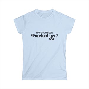 May include: Light blue t-shirt with the text "HAVE YOU BEEN Patched yet?" in black. The shirt has short sleeves and a crew neck. The text is in a playful, stylized font.